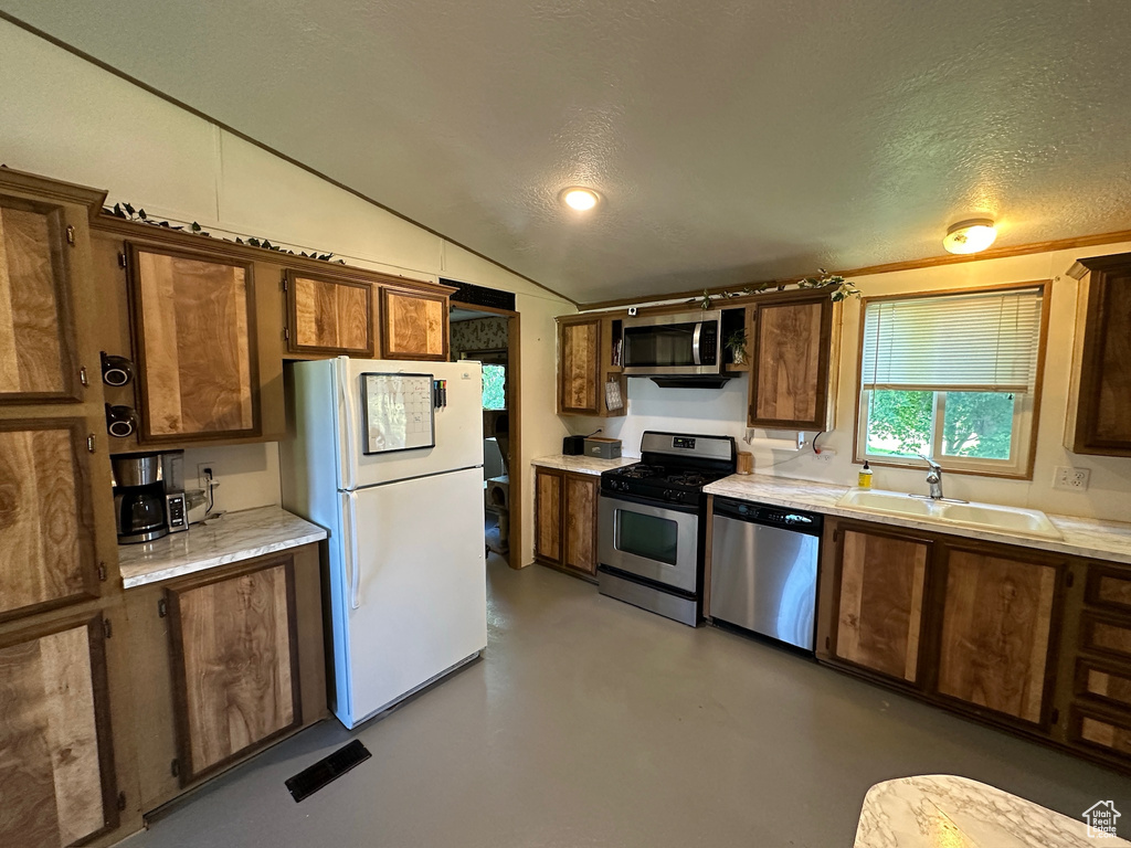 Kitchen with sink, a textured ceiling, vaulted ceiling, and stainless steel appliances