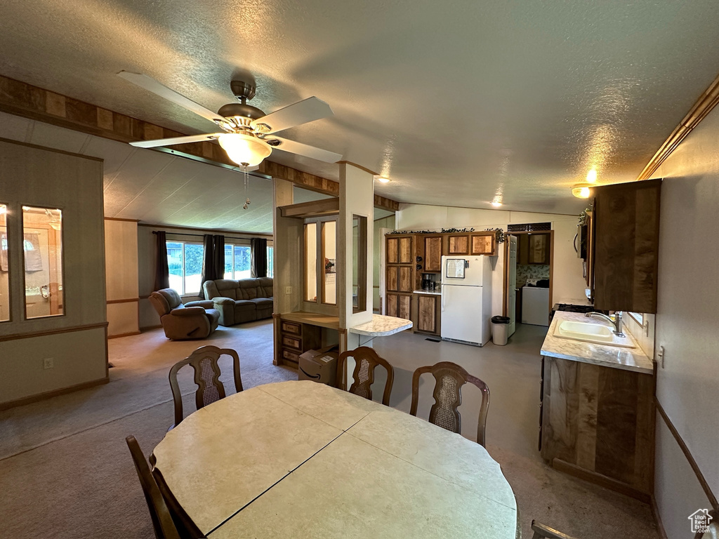 Dining area featuring washer / dryer, sink, carpet flooring, ceiling fan, and vaulted ceiling