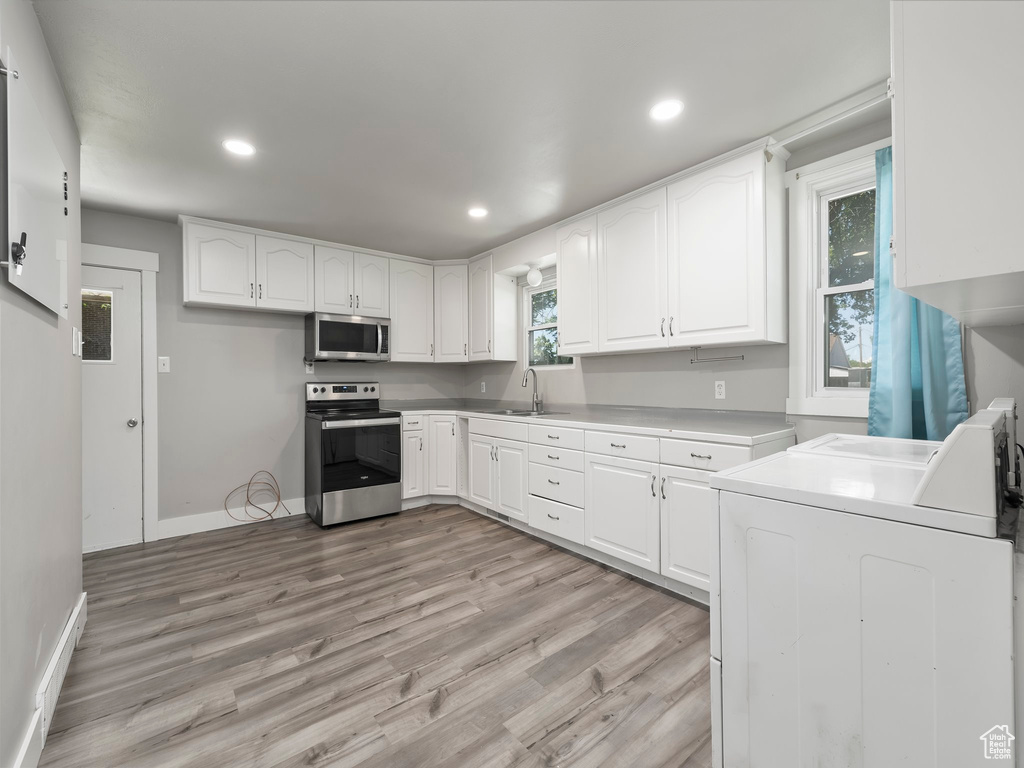 Kitchen with independent washer and dryer, stainless steel appliances, light wood-type flooring, white cabinets, and sink