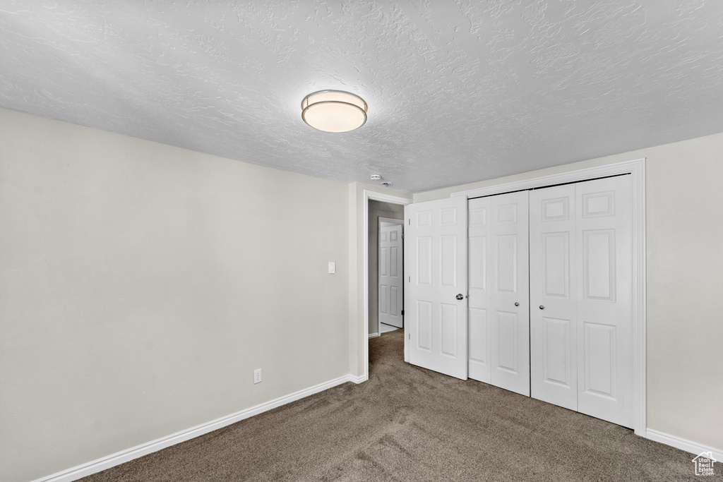 Unfurnished bedroom with a textured ceiling, a closet, and dark carpet