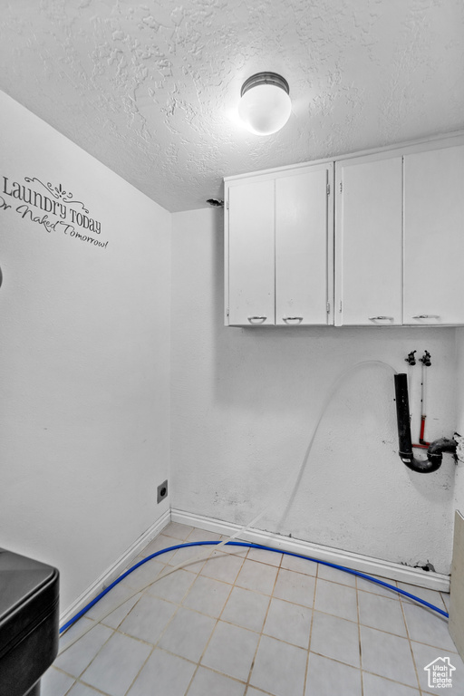 Laundry area with cabinets, a textured ceiling, light tile floors, and washer hookup