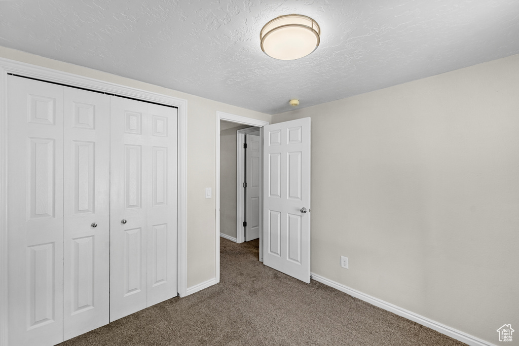 Unfurnished bedroom with a textured ceiling, a closet, and carpet