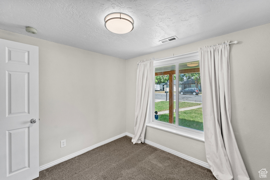 Unfurnished room with dark carpet and a textured ceiling