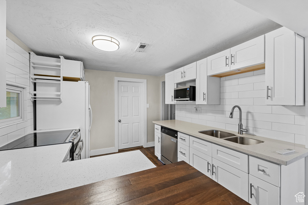 Kitchen with dark hardwood / wood-style flooring, backsplash, white cabinetry, appliances with stainless steel finishes, and sink