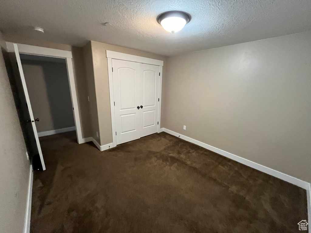 Unfurnished bedroom featuring dark colored carpet, a closet, and a textured ceiling