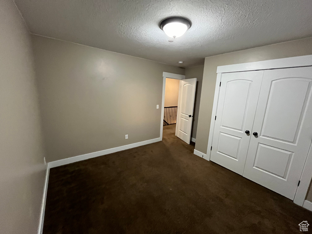 Unfurnished bedroom featuring a closet, a textured ceiling, and dark carpet