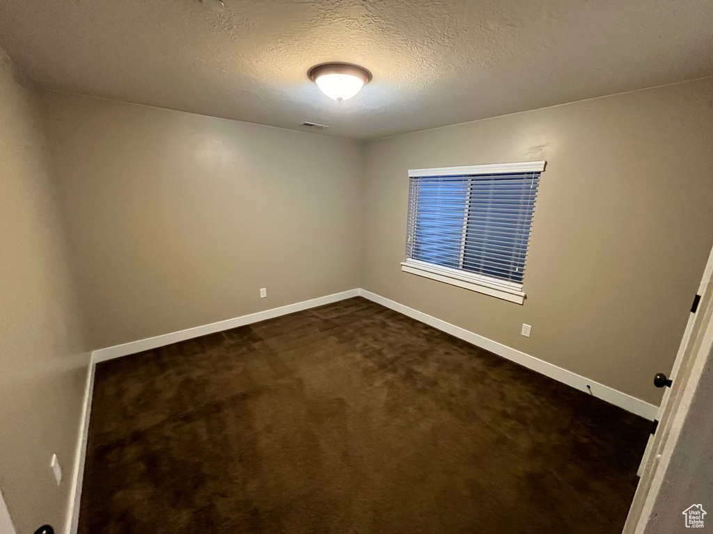 Spare room featuring a textured ceiling and dark carpet