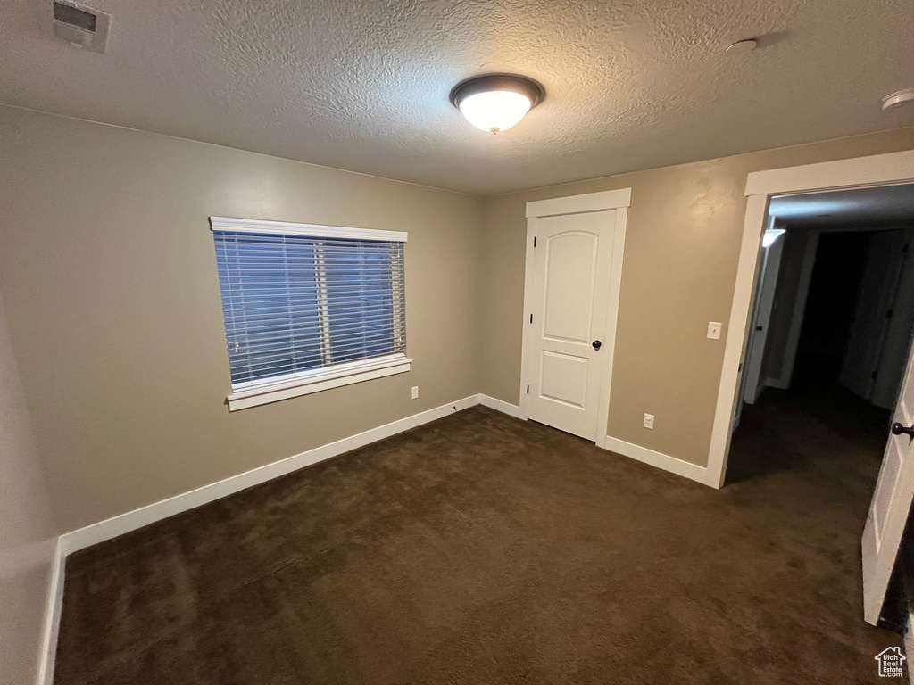 Unfurnished bedroom featuring a textured ceiling and dark colored carpet