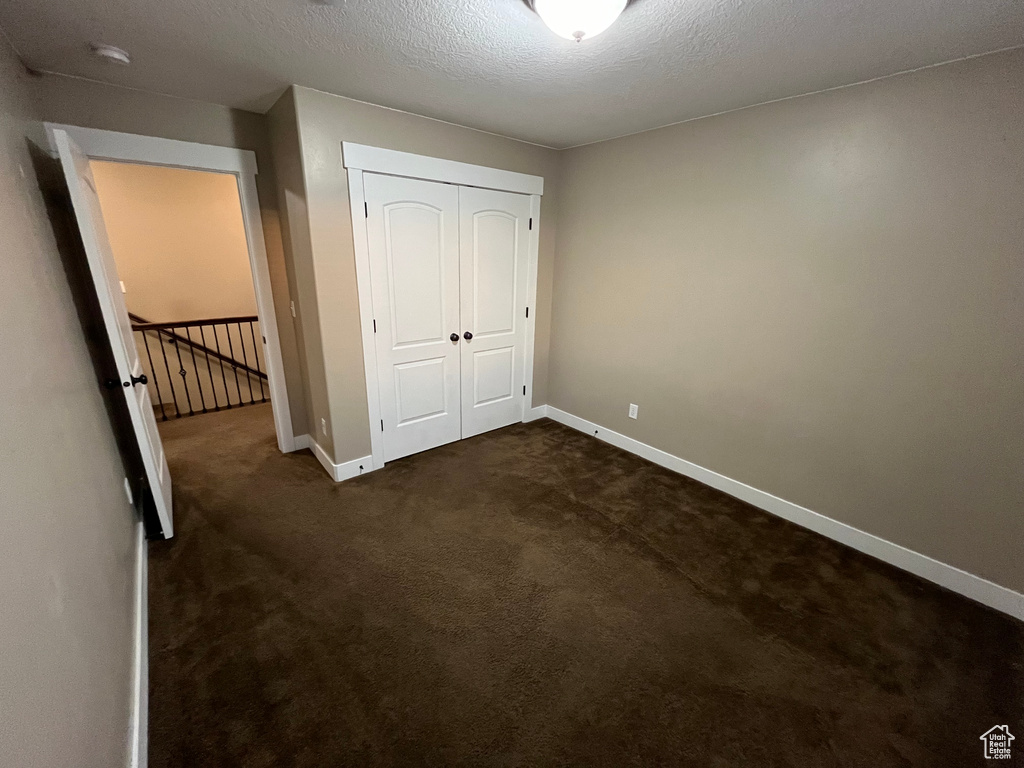 Unfurnished bedroom with a textured ceiling, a closet, and dark carpet