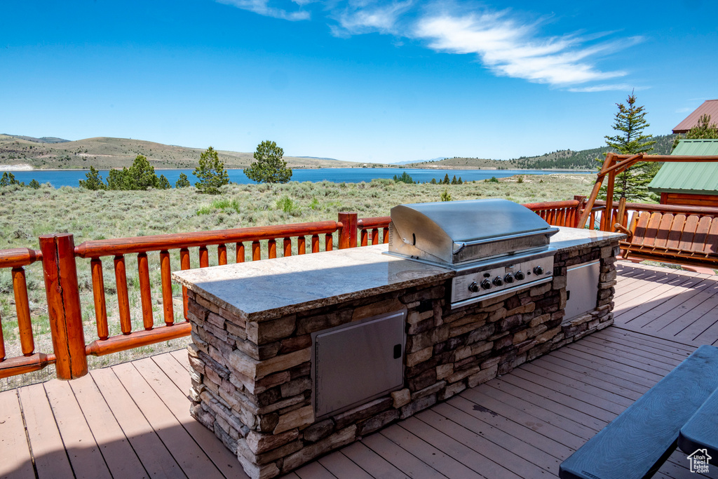 Wooden terrace featuring a water view, exterior kitchen, and a grill