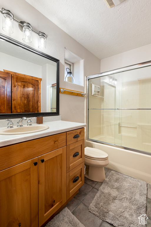 Full bathroom featuring a textured ceiling, bath / shower combo with glass door, vanity, and toilet