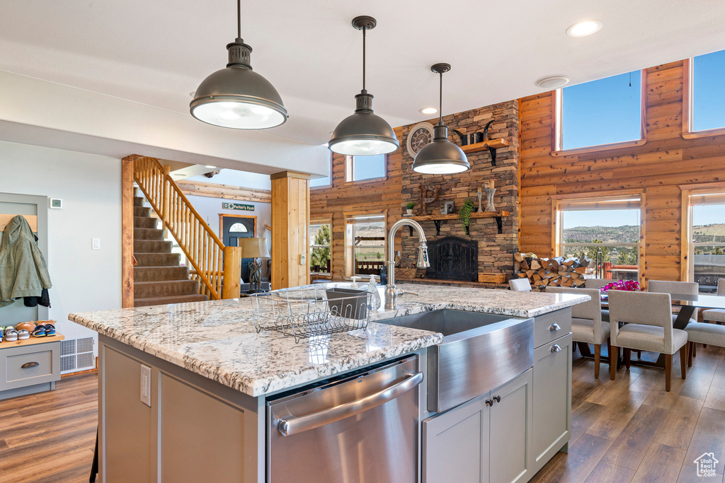 Kitchen featuring an island with sink, dark hardwood / wood-style floors, wooden walls, and stainless steel dishwasher