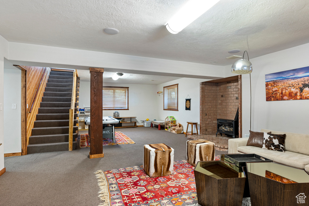 Carpeted living room with ornate columns, a textured ceiling, a wood stove, and brick wall