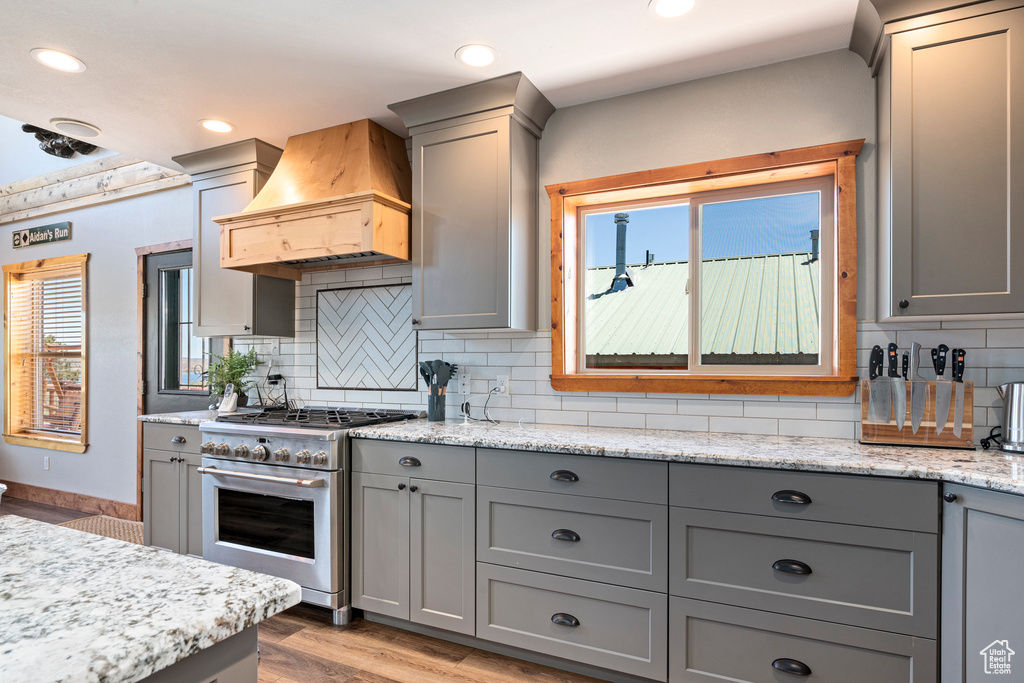 Kitchen with high end stove, premium range hood, tasteful backsplash, and light hardwood / wood-style flooring