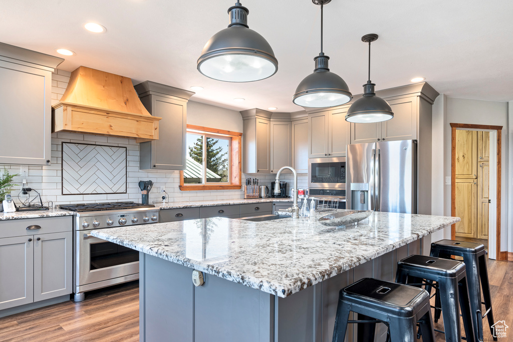 Kitchen with decorative light fixtures, light hardwood / wood-style flooring, backsplash, custom exhaust hood, and appliances with stainless steel finishes