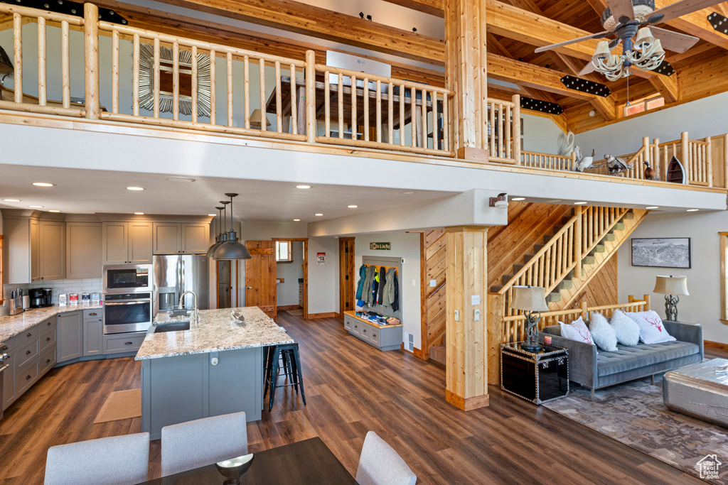 Kitchen featuring hanging light fixtures, dark wood-type flooring, stainless steel appliances, light stone counters, and a towering ceiling