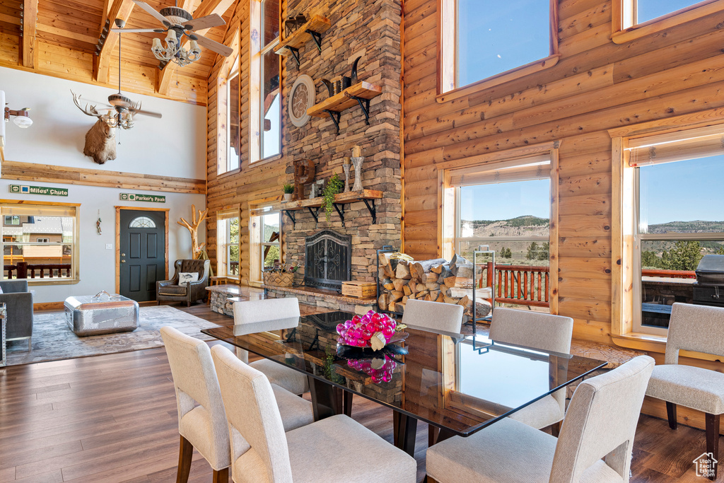 Dining room featuring ceiling fan, hardwood / wood-style floors, a stone fireplace, rustic walls, and a high ceiling