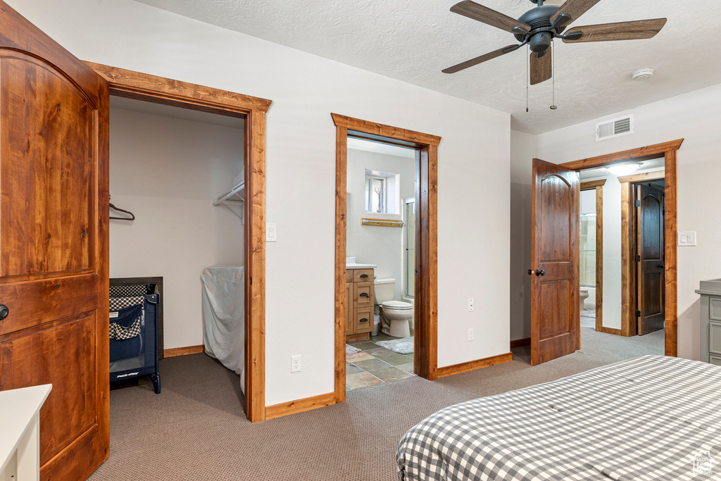 Carpeted bedroom with a closet, ceiling fan, ensuite bath, a spacious closet, and a textured ceiling