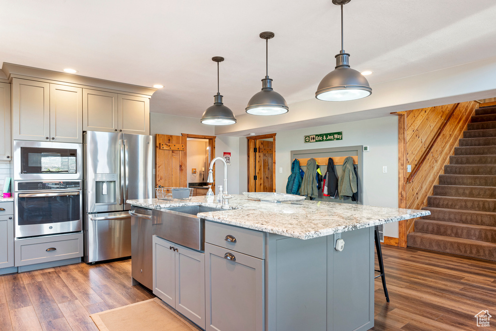 Kitchen featuring hanging light fixtures, stainless steel appliances, hardwood / wood-style floors, and a center island with sink