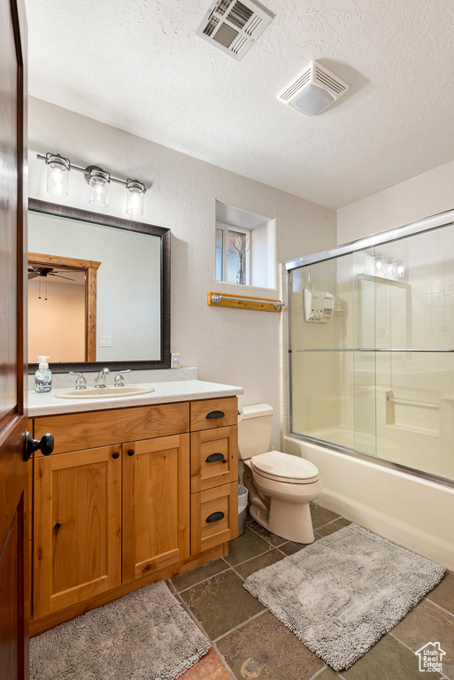 Full bathroom with a textured ceiling, enclosed tub / shower combo, tile floors, toilet, and vanity