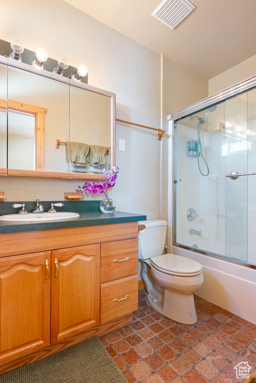 Full bathroom with tile flooring, oversized vanity, shower / bath combination with glass door, a textured ceiling, and toilet