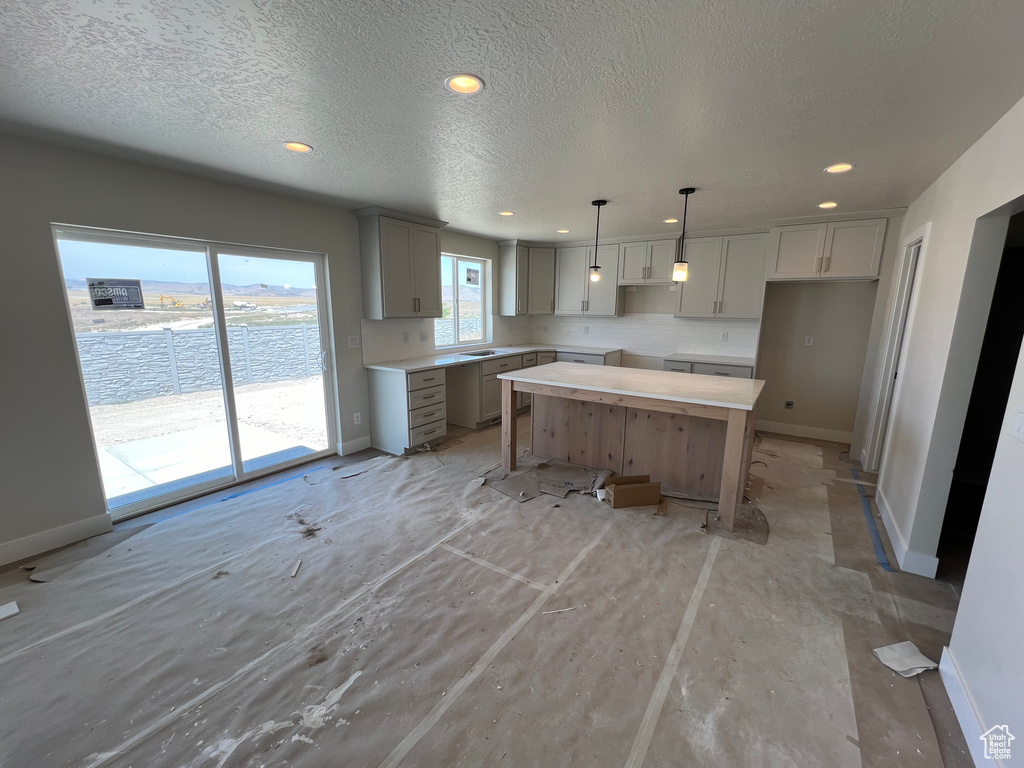 Kitchen featuring a center island, a textured ceiling, hanging light fixtures, and gray cabinetry