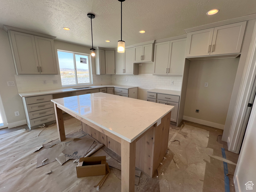 Kitchen featuring light tile patterned floors, a kitchen island, hanging light fixtures, decorative backsplash, and gray cabinetry