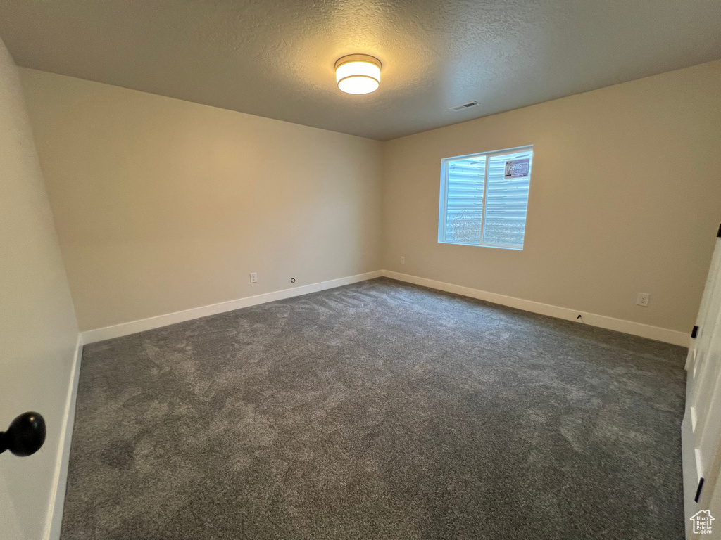 Spare room with dark carpet and a textured ceiling