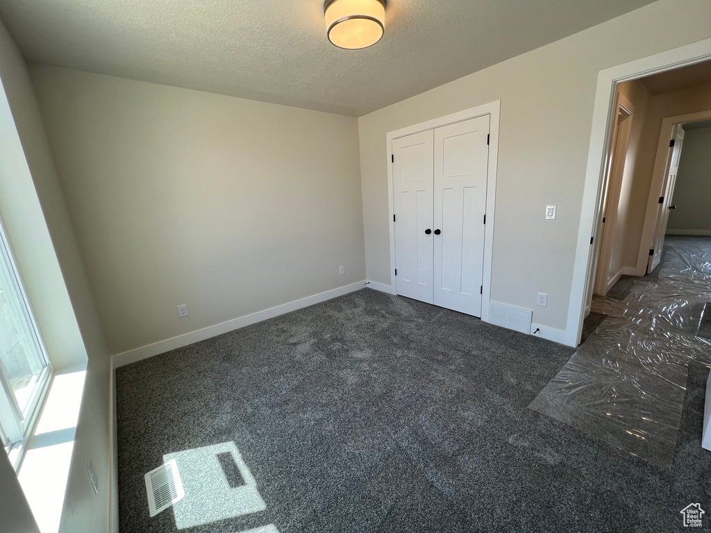 Unfurnished bedroom with dark carpet, a textured ceiling, and a closet