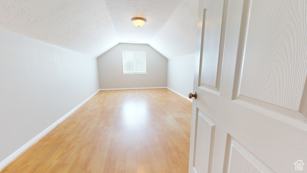 Additional living space with lofted ceiling, a textured ceiling, and light wood-type flooring