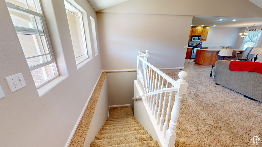 Stairs featuring light carpet, a healthy amount of sunlight, and an inviting chandelier