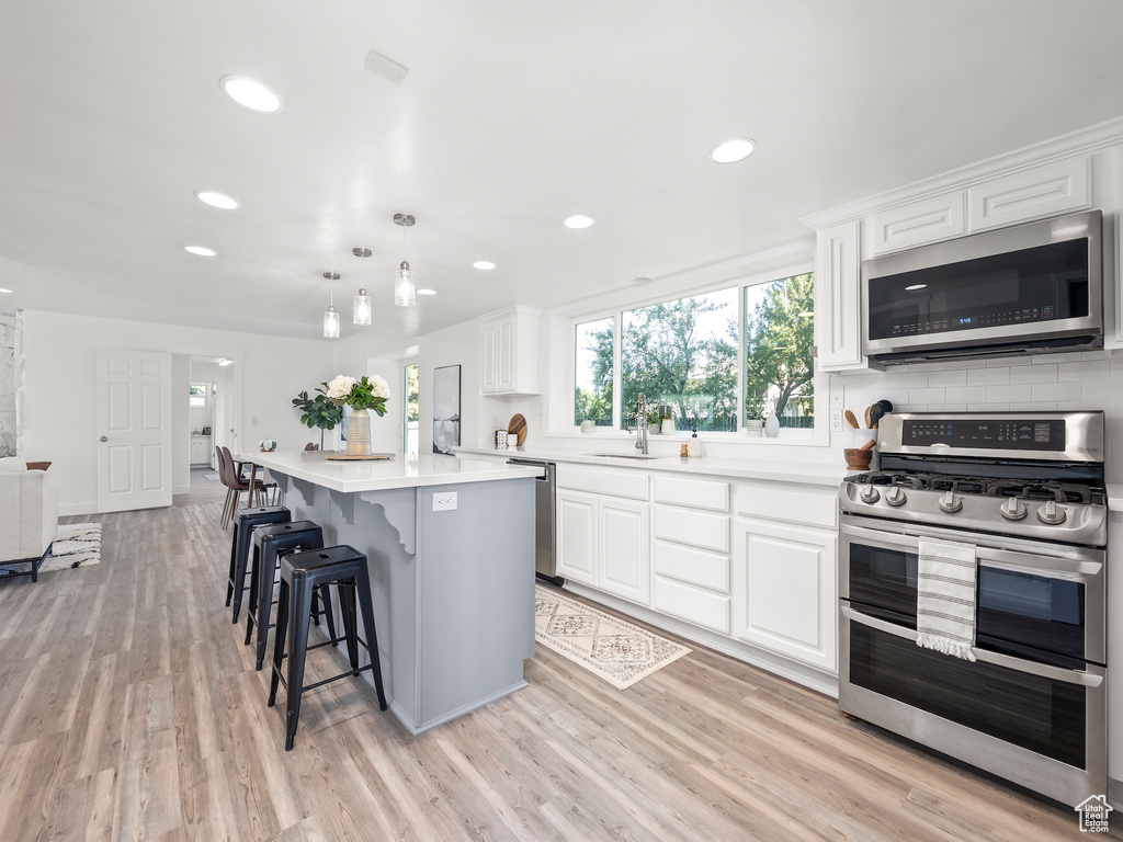 Kitchen with white cabinetry, hanging light fixtures, light hardwood / wood-style flooring, stainless steel appliances, and a breakfast bar area