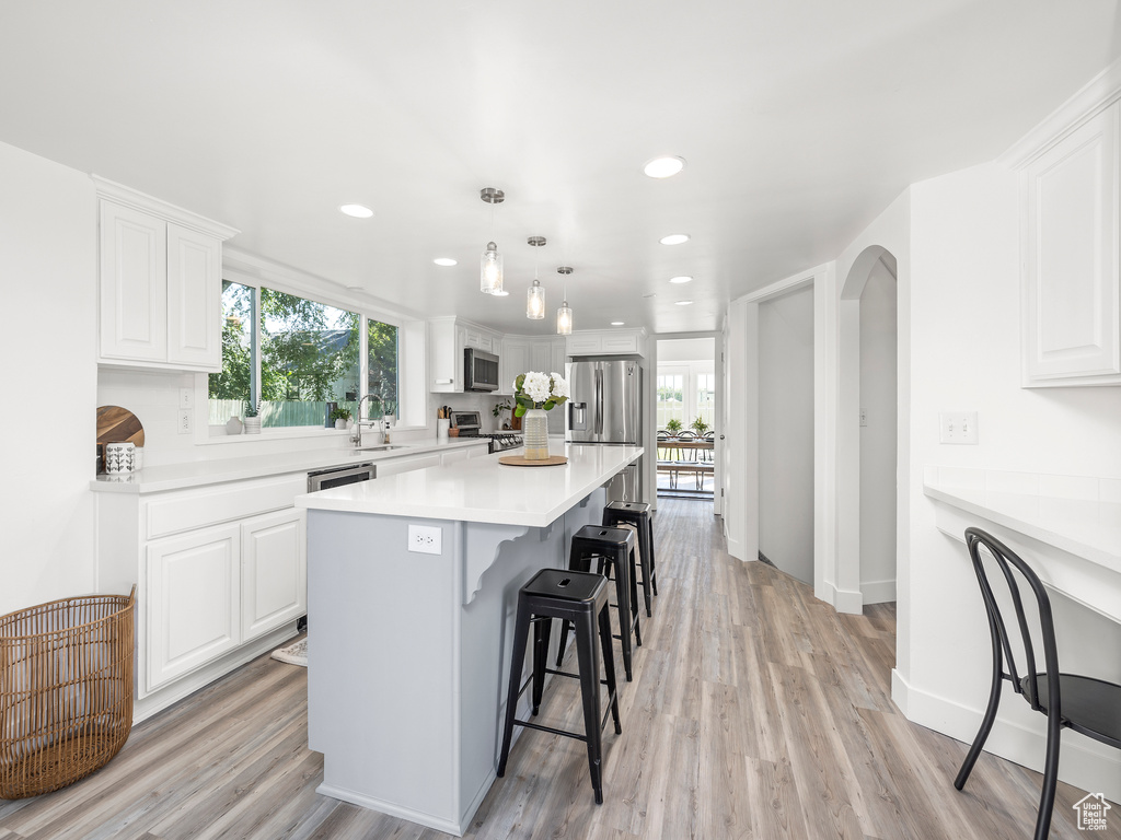 Kitchen with decorative light fixtures, stainless steel appliances, a center island, light wood-type flooring, and white cabinets