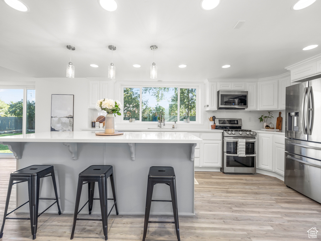 Kitchen with light hardwood / wood-style flooring, decorative light fixtures, a kitchen bar, white cabinetry, and appliances with stainless steel finishes