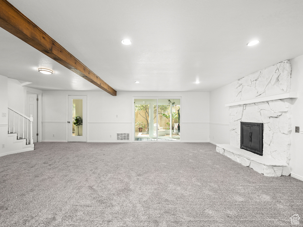 Unfurnished living room with a stone fireplace, carpet, and beamed ceiling