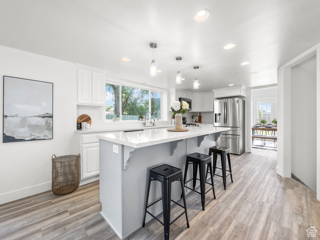 Kitchen with decorative light fixtures, stainless steel refrigerator with ice dispenser, light wood-type flooring, a kitchen island, and white cabinetry