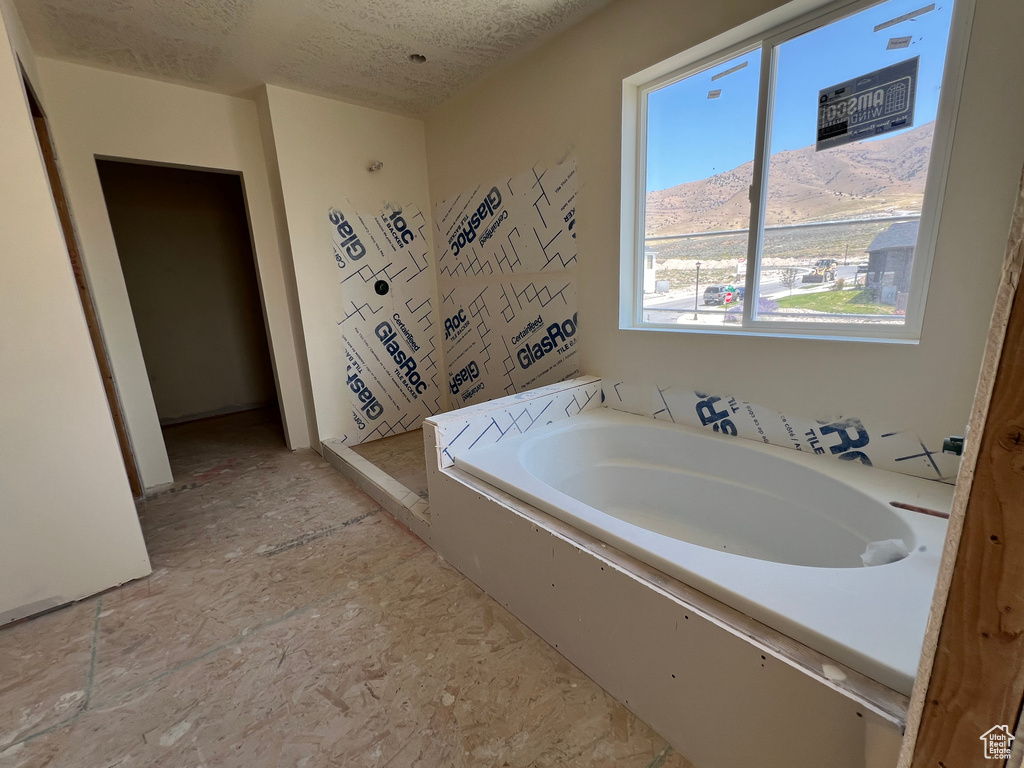 Bathroom featuring a textured ceiling, a tub to relax in, and tile patterned floors