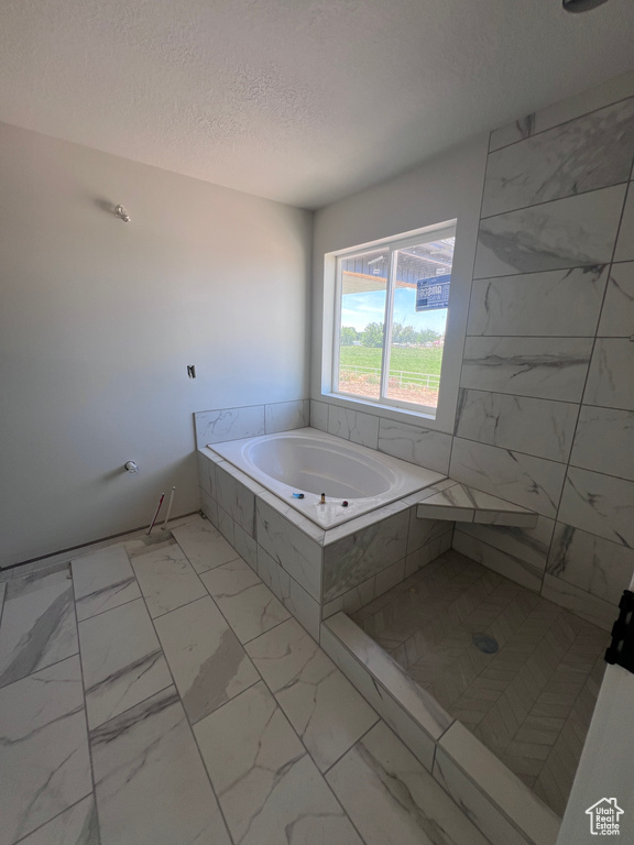 Bathroom with tile floors, a relaxing tiled bath, and a textured ceiling