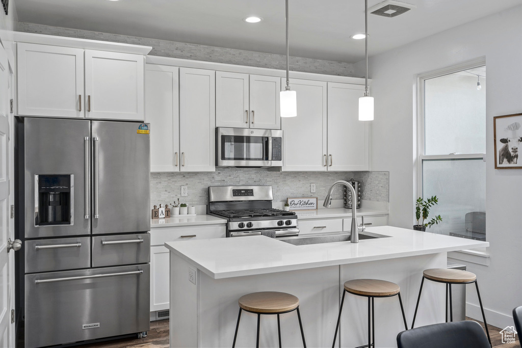 Kitchen featuring decorative light fixtures, sink, white cabinetry, and stainless steel appliances