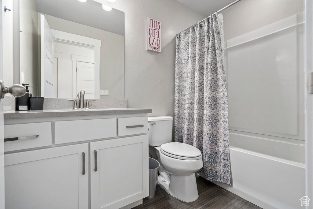 Full bathroom with toilet, hardwood / wood-style flooring, shower / bathtub combination with curtain, and vanity