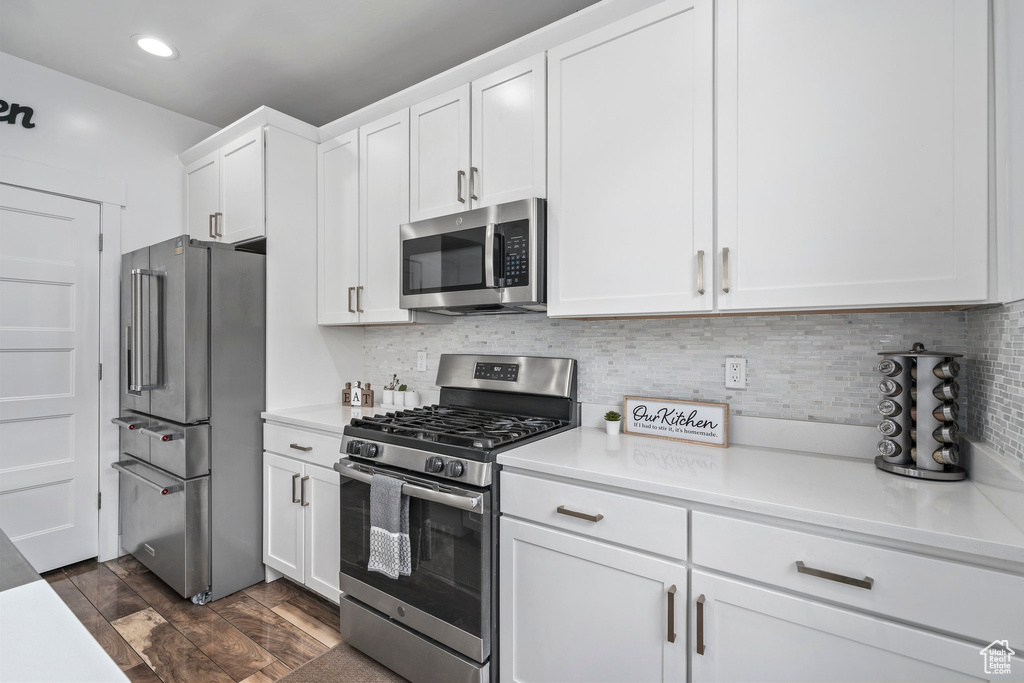 Kitchen featuring appliances with stainless steel finishes, white cabinets, backsplash, and dark hardwood / wood-style flooring