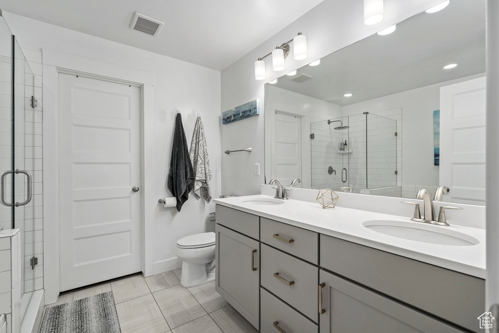 Bathroom with a shower with shower door, large vanity, tile floors, and dual sinks