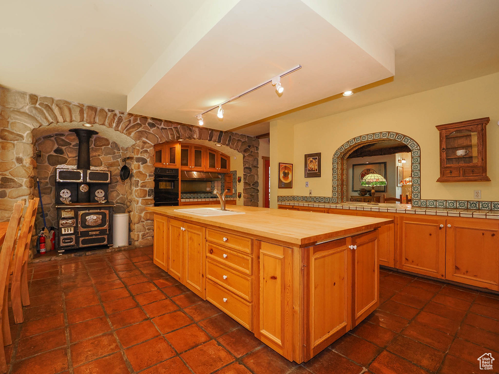 Kitchen with a center island with sink, butcher block countertops, a wood stove, track lighting, and dark tile floors