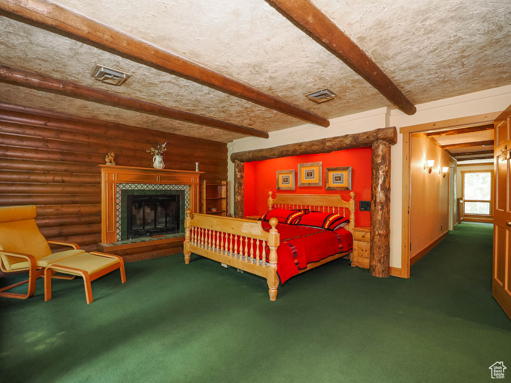 Carpeted bedroom featuring beam ceiling, a tile fireplace, a textured ceiling, and rustic walls