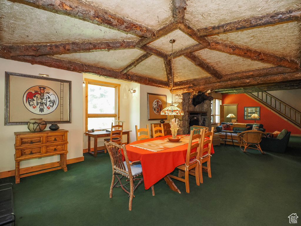 Carpeted dining room featuring beamed ceiling and a stone fireplace