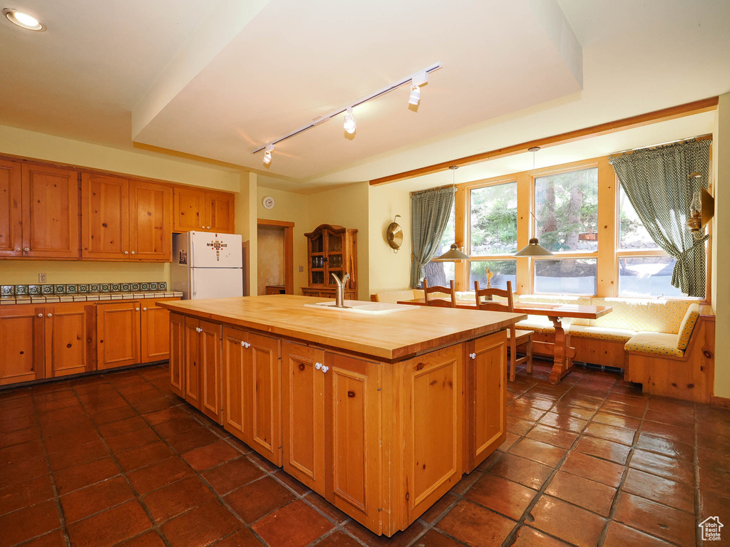 Kitchen with a center island with sink, butcher block counters, white refrigerator, sink, and dark tile floors