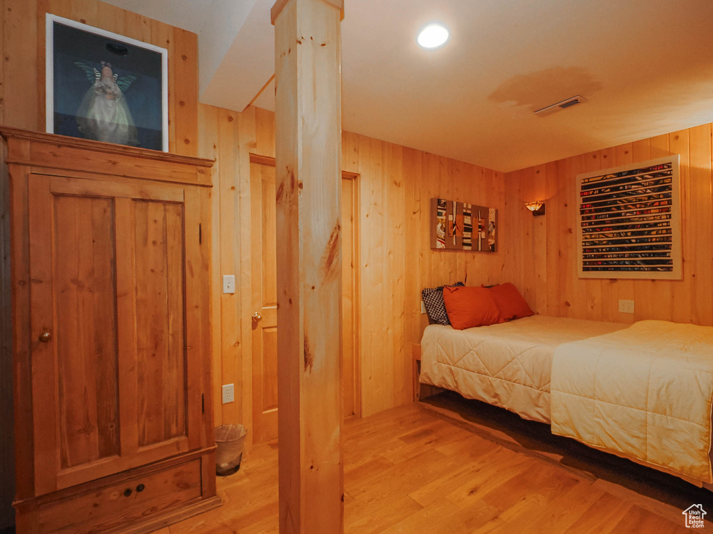 Bedroom with wooden walls, light hardwood / wood-style floors, and ornate columns