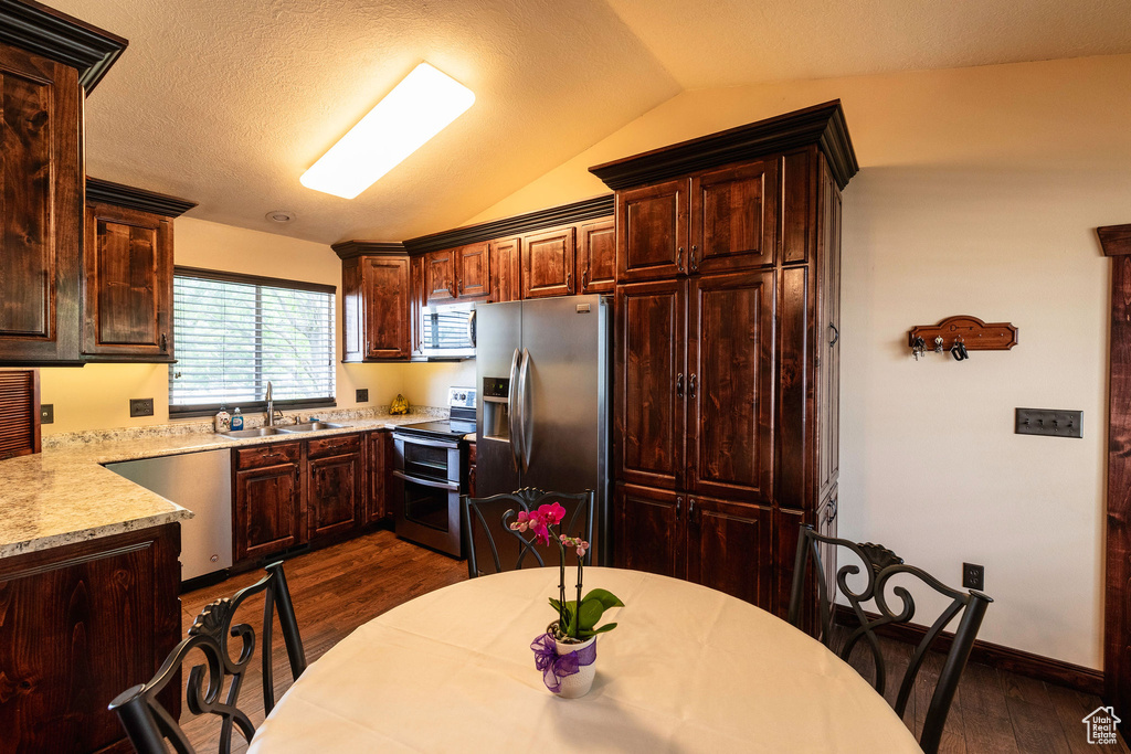 Kitchen featuring stainless steel appliances, vaulted ceiling, dark brown cabinetry, dark hardwood / wood-style flooring, and sink