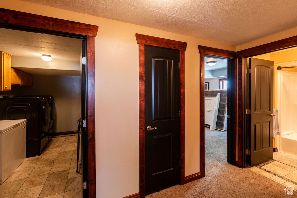 Hallway featuring washer and dryer, light carpet, and a textured ceiling