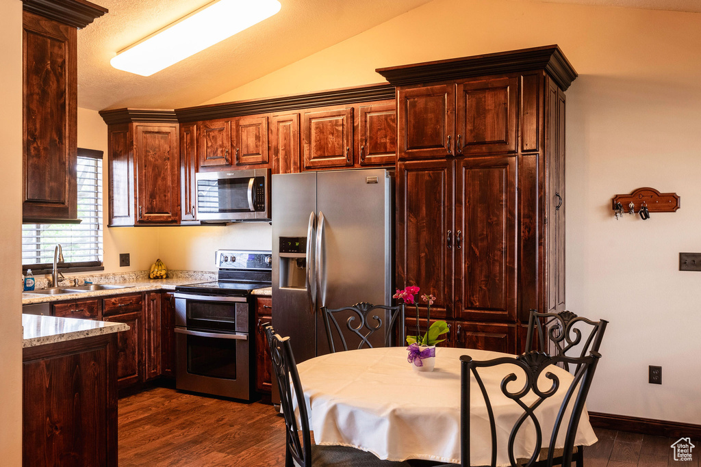 Kitchen featuring appliances with stainless steel finishes, sink, dark wood-type flooring, and vaulted ceiling